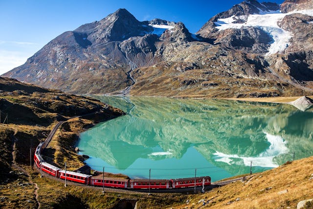 Warum denn in die Ferne schweifen, wenn man in der Schweiz ein Bahnlinie hat, die seit 2008 zum Unesco-Welterbe zählt? Eine Zugkomposition der Rhätischen Bahn kurvt um den Lago Bianco am Berninapass.