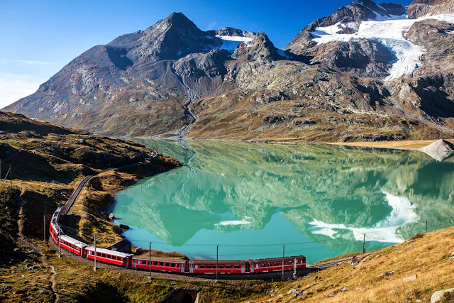 Warum denn in die Ferne schweifen, wenn man in der Schweiz ein Bahnlinie hat, die seit 2008 zum Unesco-Welterbe zählt? Eine Zugkomposition der Rhätischen Bahn kurvt um den Lago Bianco am Berninapass.
