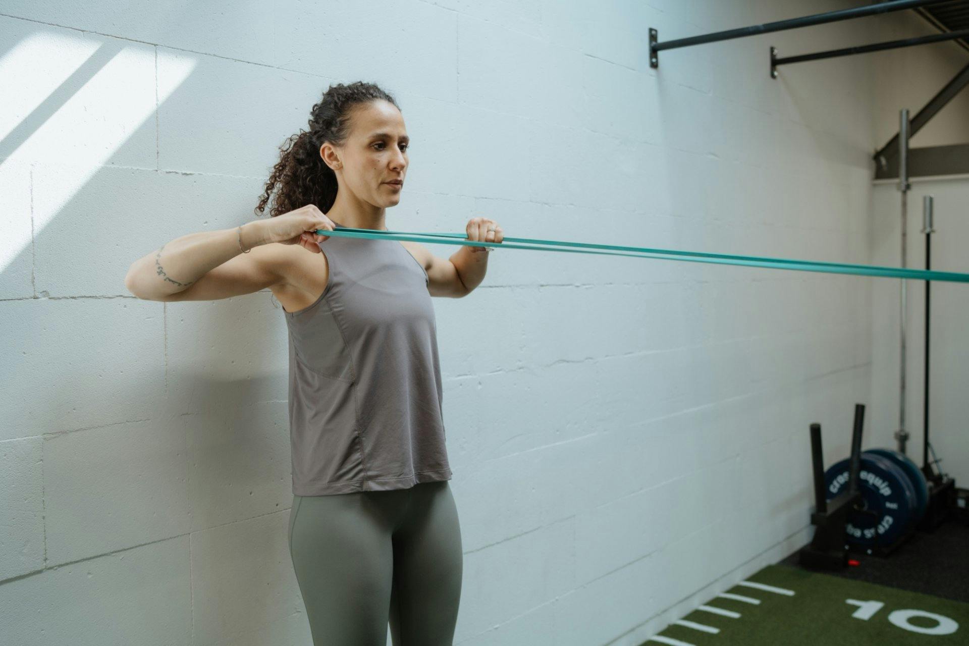 Facepull: Widerstandsband auf Schulterhöhe fixieren, Enden mit beiden Händen greifen, Ellbogen nach hinten ziehen, Schulterblätter zusammenführen. Stä...