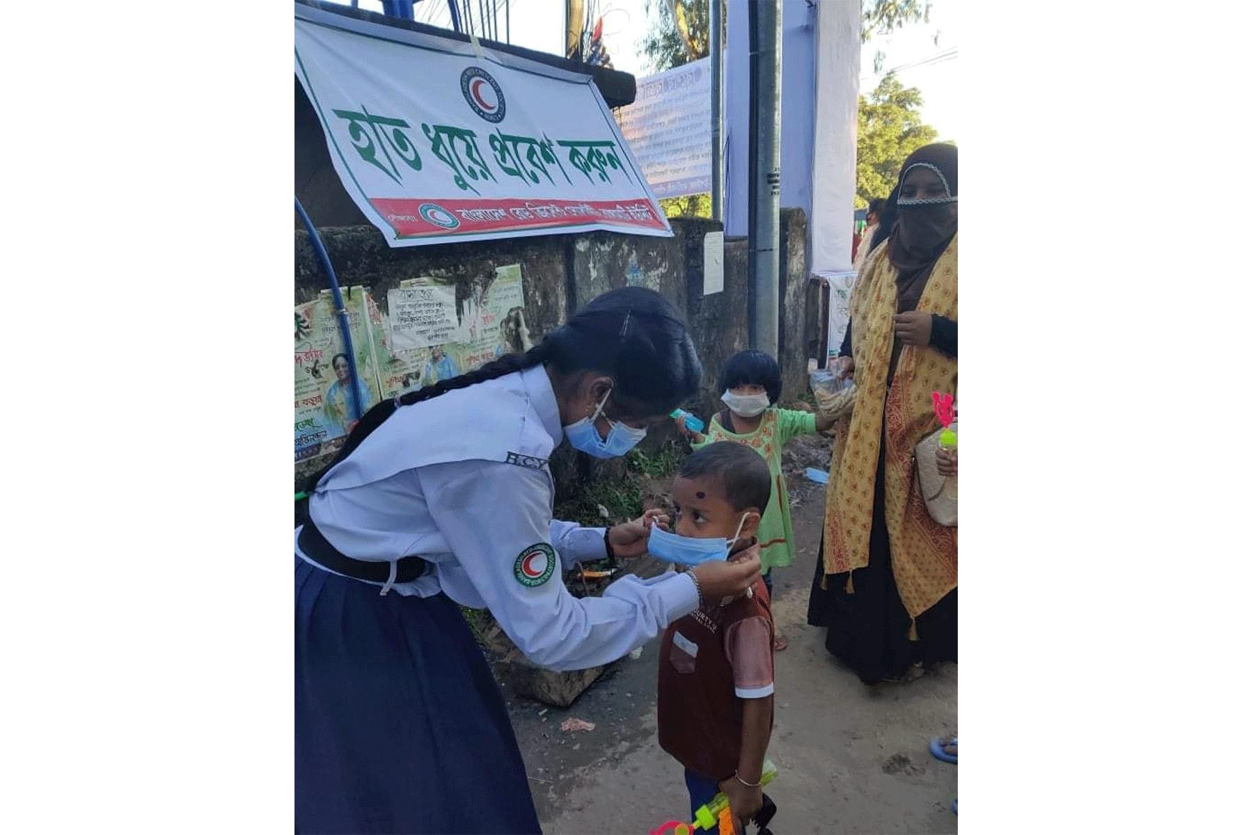 Eine Freiwillige des Roten Halbmondes Bangladesch zeigt einem Kind, wie es seine Maske richtig anlegt, um sich vor dem Coronavirus zu schützen.