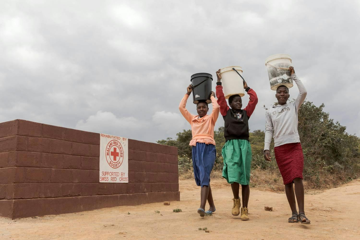 Malawische Schülerinnen holen Wasser für den Schulgarten – die Wasserstelle bei der Schule hat das Schweizerische Rote Kreuz wieder in Stand gestellt.